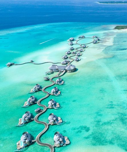 Exotisches Überwasser-Resort auf den Malediven mit geschwungenen Stegen und Villen im türkisfarbenen Ozean aus der Vogelperspektive. Exotisches Überwasser-Resort auf den Malediven mit geschwungenen Stegen und Villen im türkisfarbenen Ozean aus der Vogelperspektive.